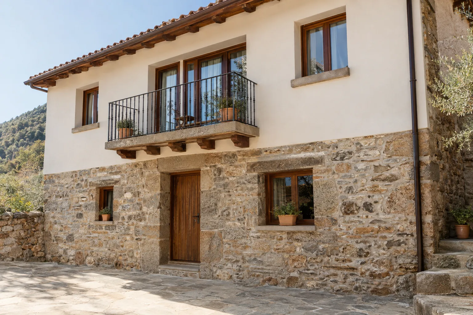 Fachada rural rehabilitada con zócalo de mampostería y balcón de forja
